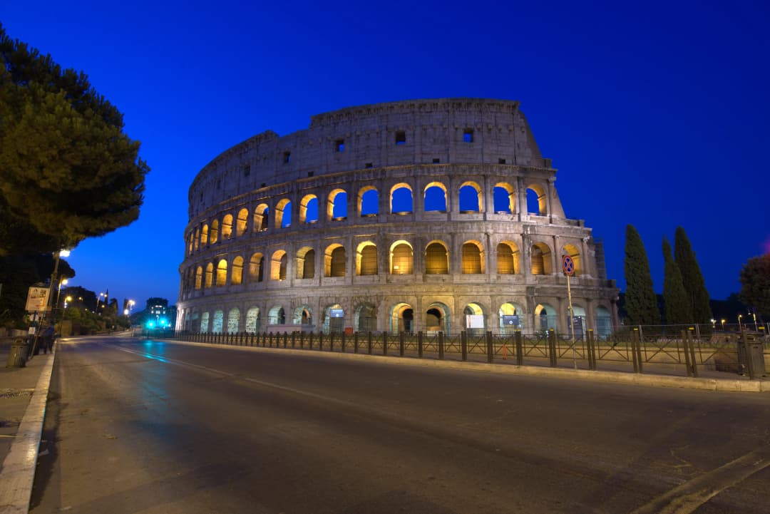 the Roman Colosseum at night backed by a deep blue sky
